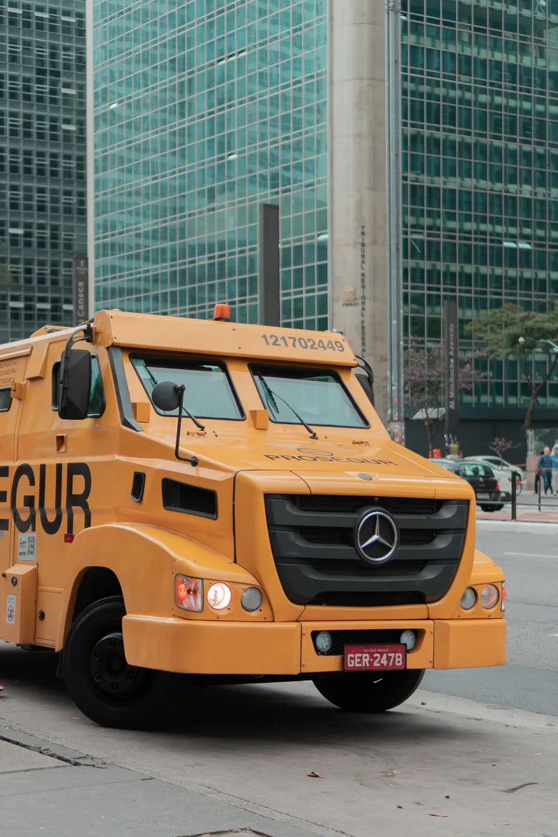 A yellow armoured cash-in-transit truck parked in a financial district