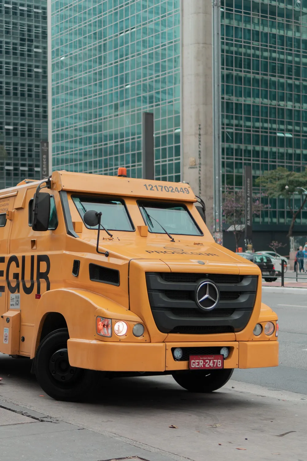 A yellow armoured cash-in-transit truck parked in a financial district