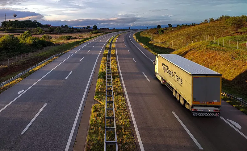 An articulated freight truck travelling along a motorway at dusk